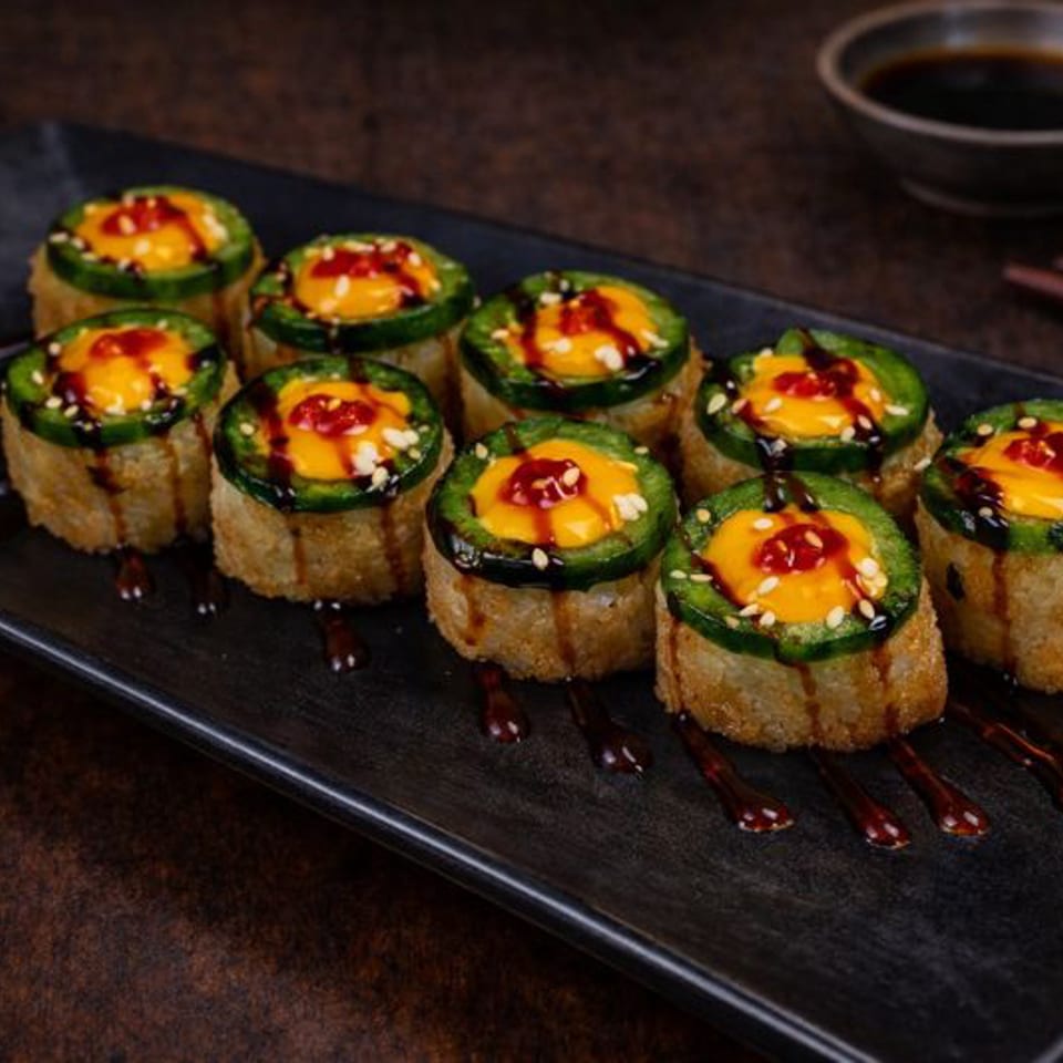 Ten fried sushi rolls topped with jalapeño, orange sauce, sesame seeds, and dark drizzle.
