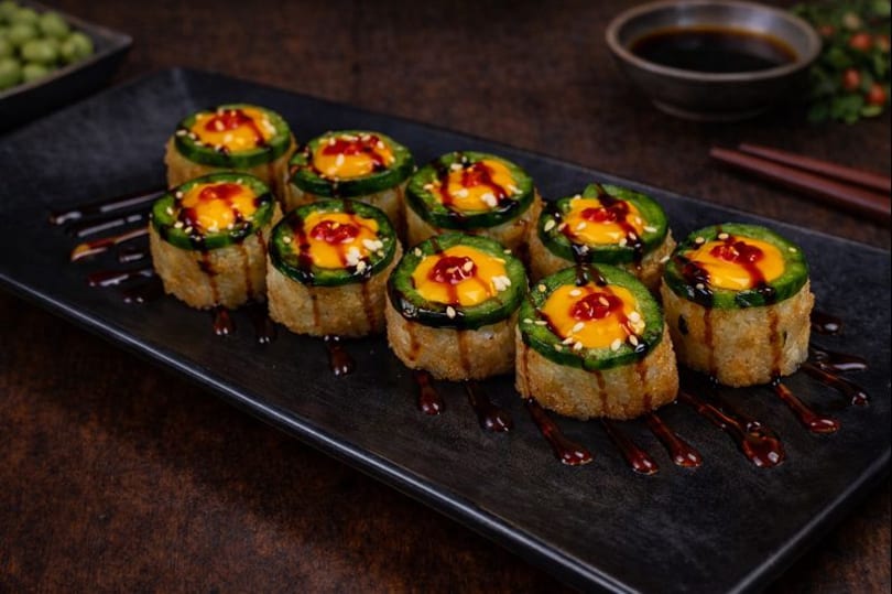 Ten fried sushi rolls topped with jalapeño, orange sauce, sesame seeds, and dark drizzle.