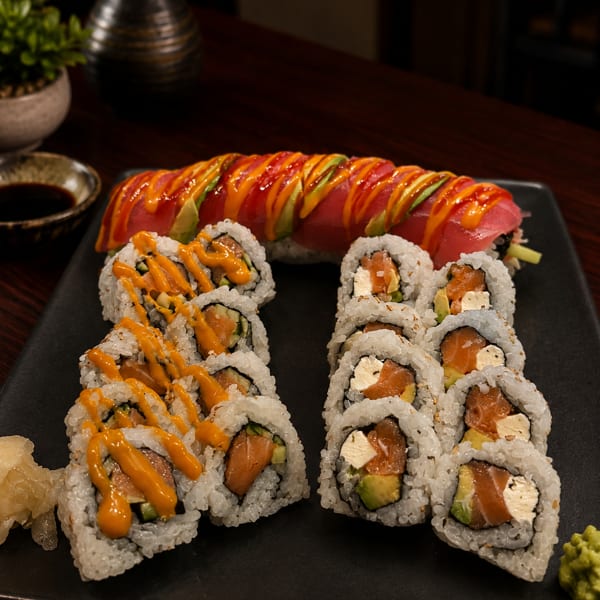 A black platter holds three types of sushi rolls, including a dragon roll with avocado and tuna.